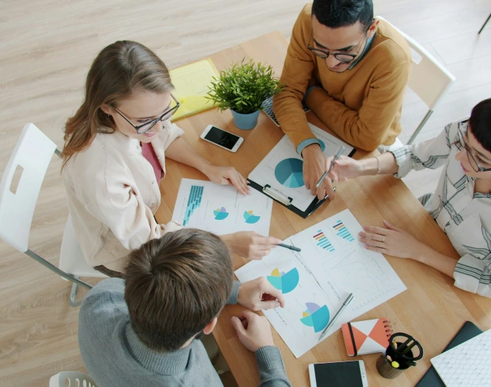 Four people collaborating around a table with charts.